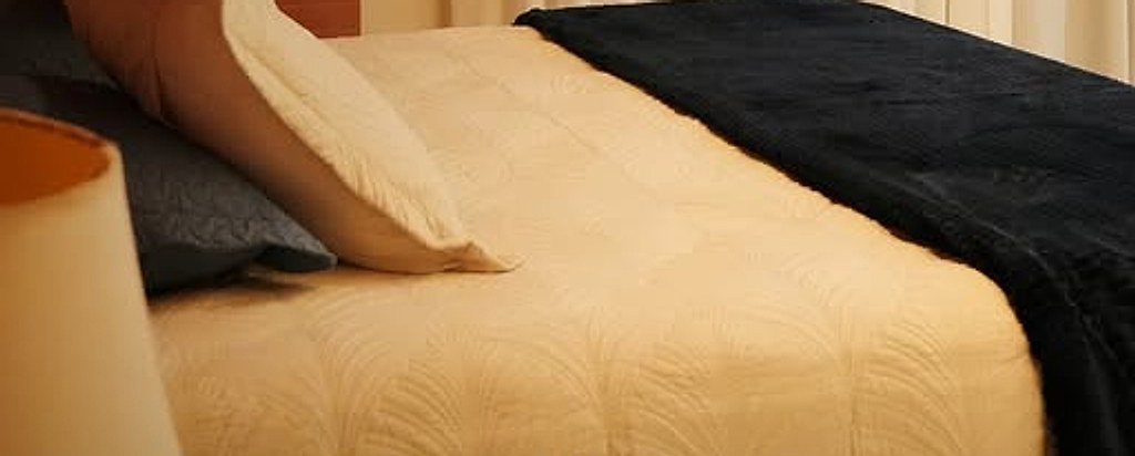 Cama de casal com manta azul-marinho e cortinas claras